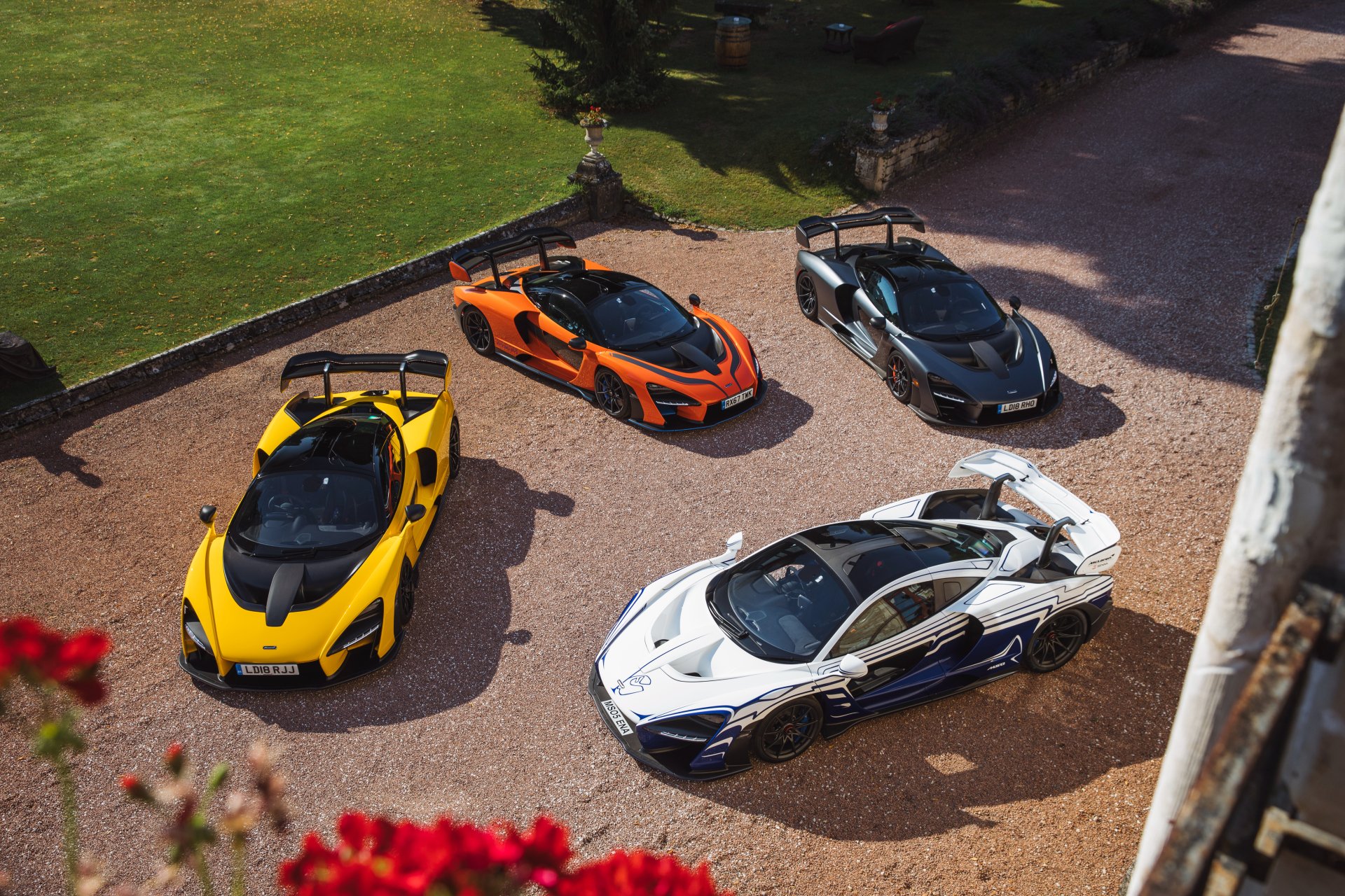 Aerial view of four McLaren Senna supercars in yellow, orange, black, and white parked on a driveway, captured in 4K ultra HD quality.