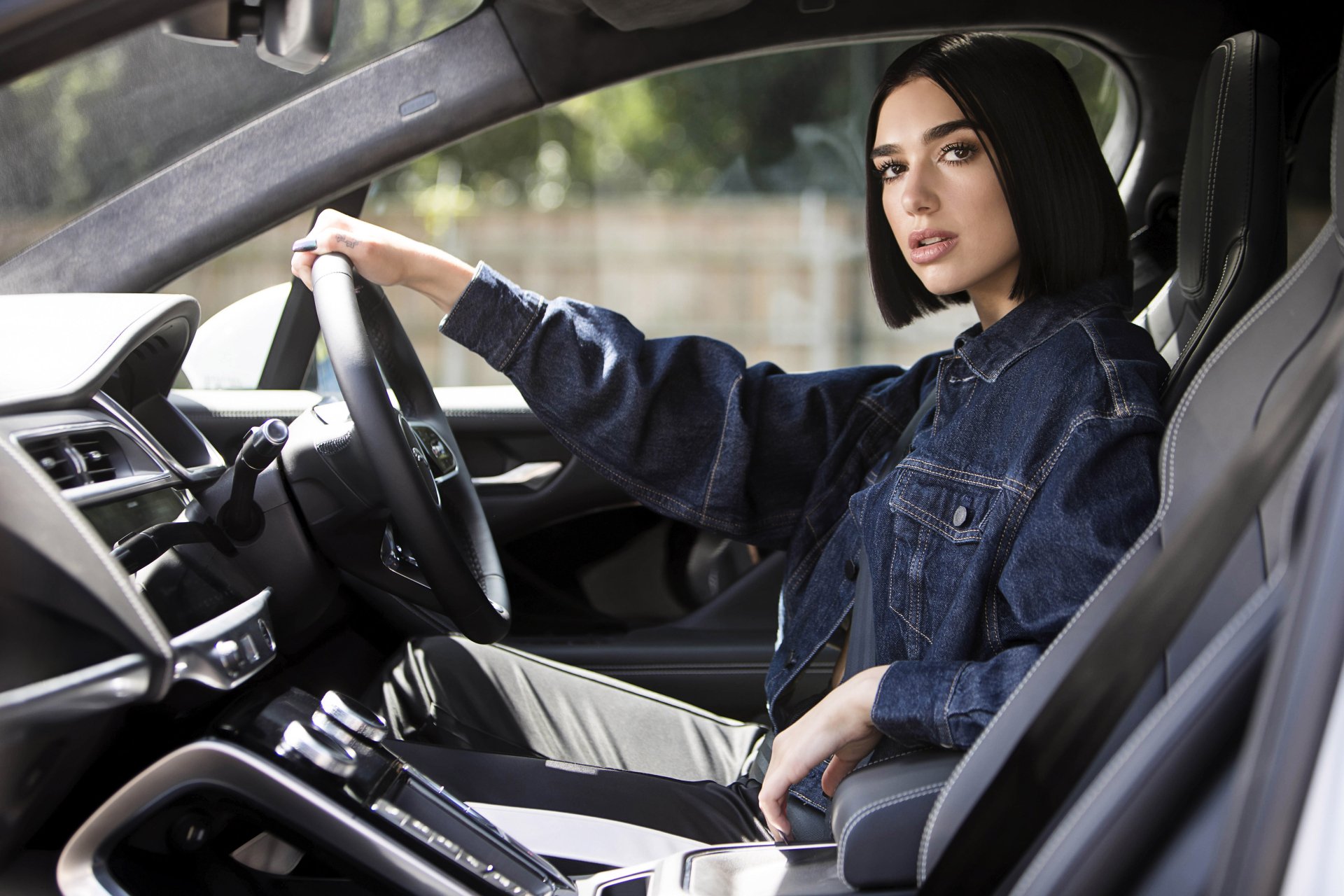 Dua Lipa sits confidently in the driver's seat of a modern car, captured in a sharp 4K Ultra HD PC desktop wallpaper blending music and automotive style.