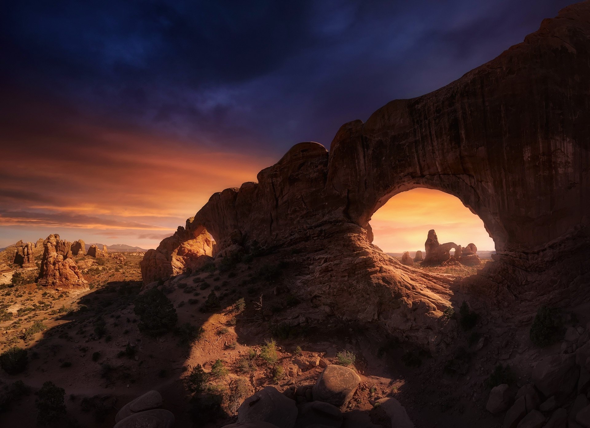 HD PC desktop wallpaper featuring a dramatic desert landscape with natural rock arches under a vibrant sunset sky.