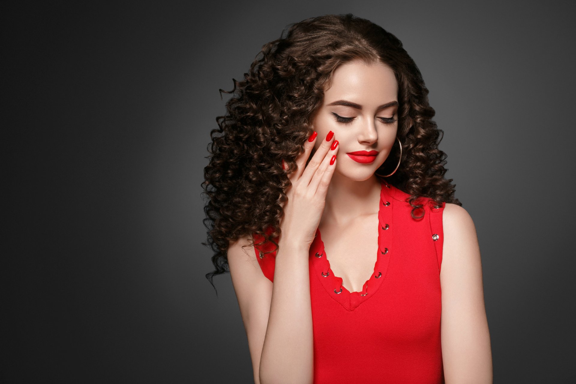 Brunette model with voluminous curls and red lipstick poses moodily against a dark background in this HD PC desktop wallpaper.