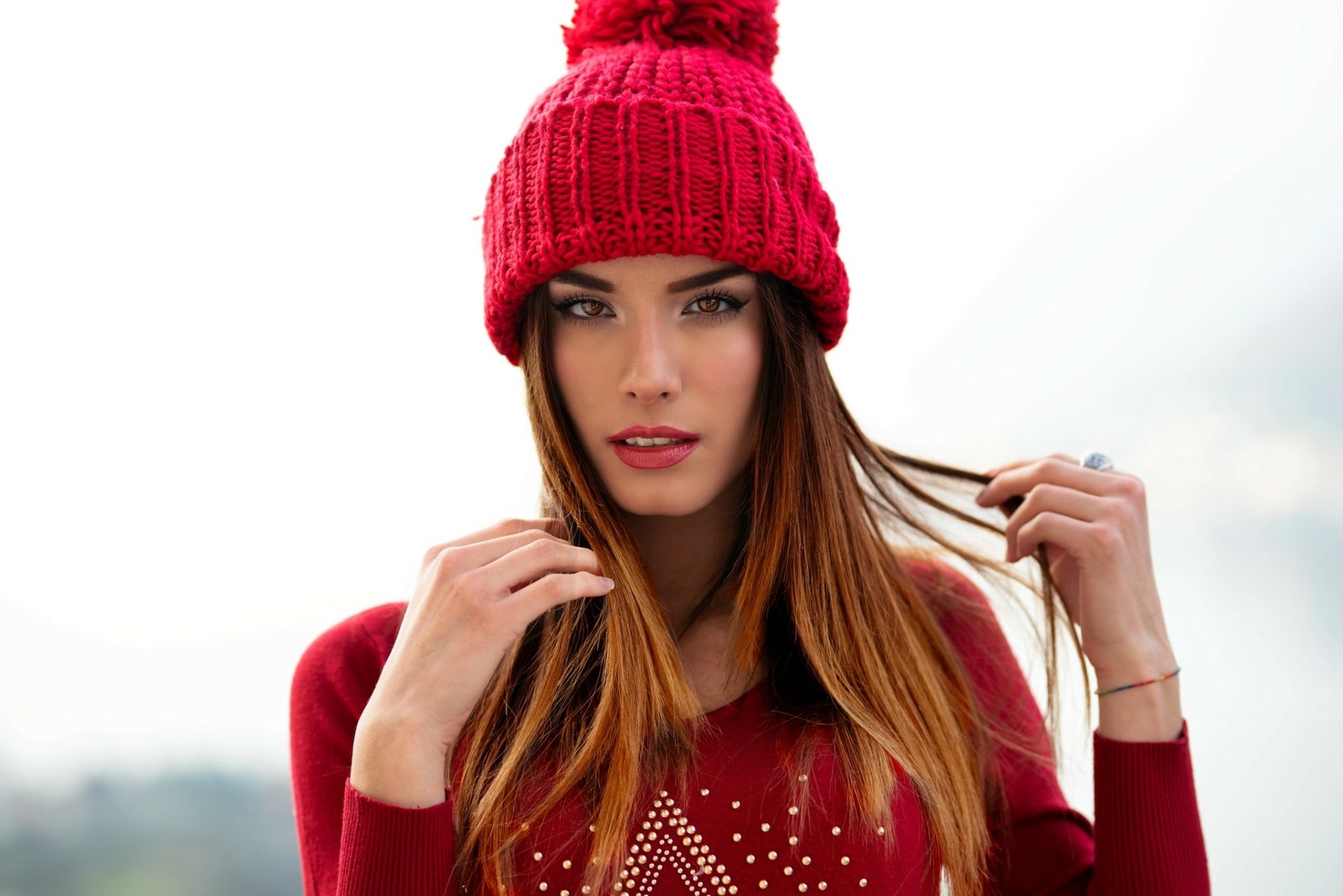 HD desktop wallpaper of a redhead model with brown eyes and lipstick, wearing a red knit hat and matching sweater, posing against a soft, out-of-focus background.