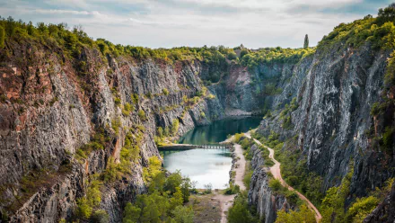A stunning 4K Ultra HD desktop wallpaper featuring a serene quarry surrounded by rugged cliffs and lush nature under a partly cloudy sky.