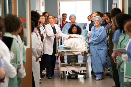 HD desktop wallpaper featuring a scene from Grey's Anatomy with the cast in a hospital corridor around a patient on a gurney.