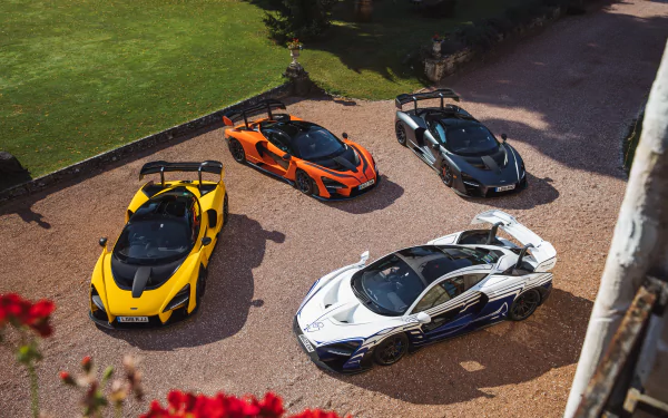 Aerial view of four McLaren Senna supercars in yellow, orange, black, and white parked on a driveway, captured in 4K ultra HD quality.