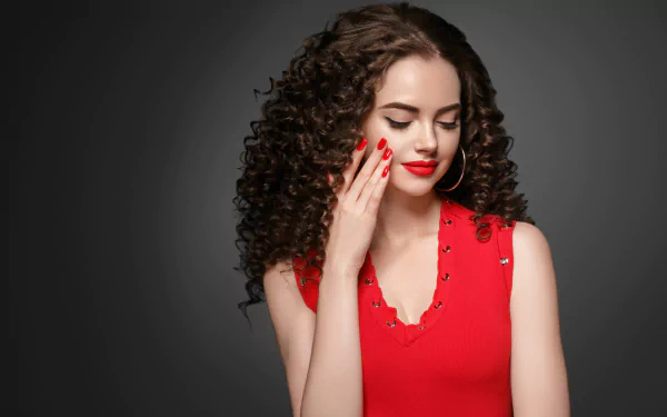Brunette model with voluminous curls and red lipstick poses moodily against a dark background in this HD PC desktop wallpaper.