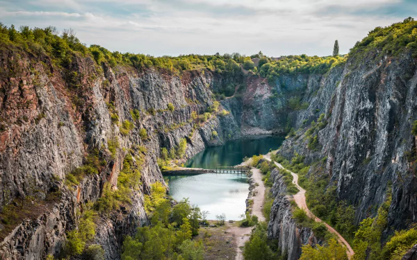 A stunning 4K Ultra HD desktop wallpaper featuring a serene quarry surrounded by rugged cliffs and lush nature under a partly cloudy sky.