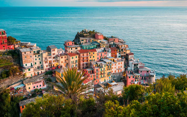 A vibrant 4K Ultra HD view of Manarola, Italy, showcasing colorful buildings along the coastline with the ocean and horizon in the background.