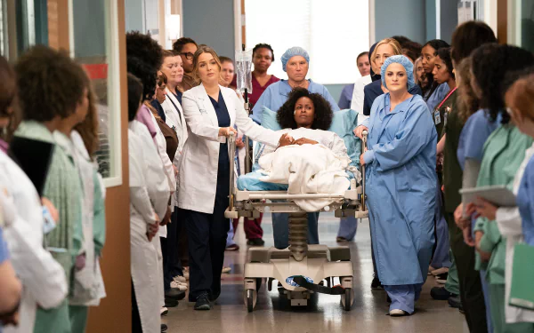 HD desktop wallpaper featuring a scene from Grey's Anatomy with the cast in a hospital corridor around a patient on a gurney.