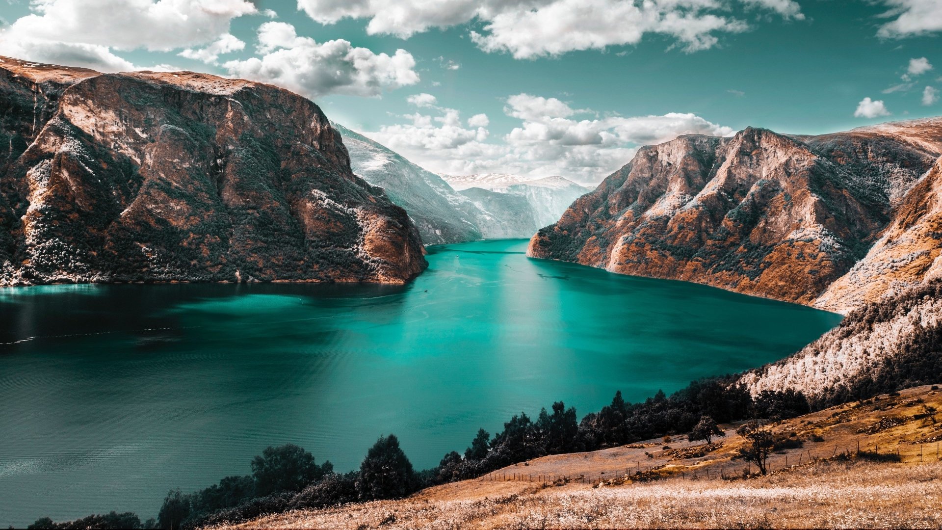 HD desktop wallpaper featuring a serene lake surrounded by towering mountains under a partly cloudy sky, capturing the essence of nature's tranquility.