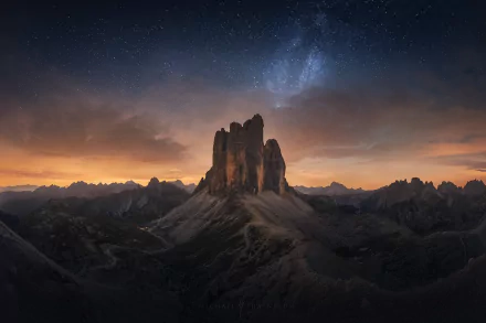 HD desktop wallpaper of Tre Cime di Lavaredo in the Dolomites, Italy, at sunset with a starry night sky and Milky Way above rugged mountain peaks.