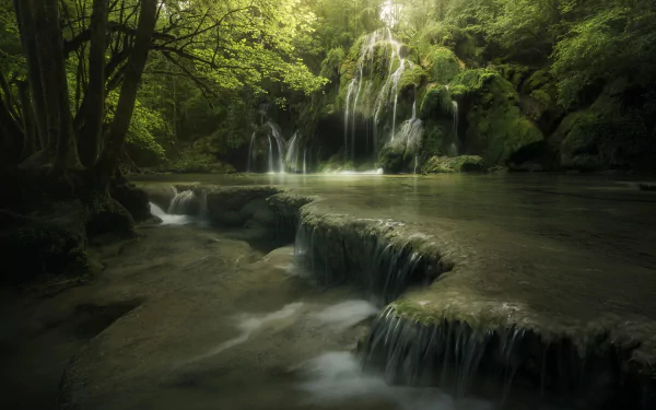 HD PC desktop wallpaper showing a serene waterfall surrounded by lush greenery and dense forest under soft sunlight filtering through the trees.