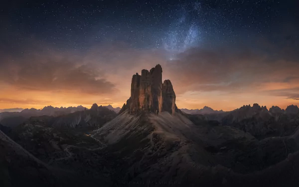 HD desktop wallpaper of Tre Cime di Lavaredo in the Dolomites, Italy, at sunset with a starry night sky and Milky Way above rugged mountain peaks.