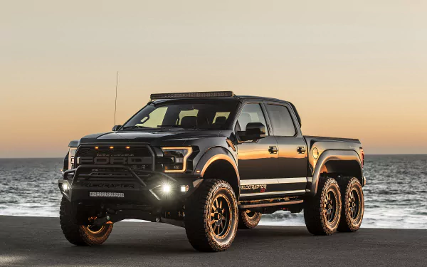 Black Hennessey VelociRaptor 6X6 Ford Raptor truck parked by the ocean at sunset, showcasing its rugged tuning and six-wheel design in a HD desktop wallpaper.