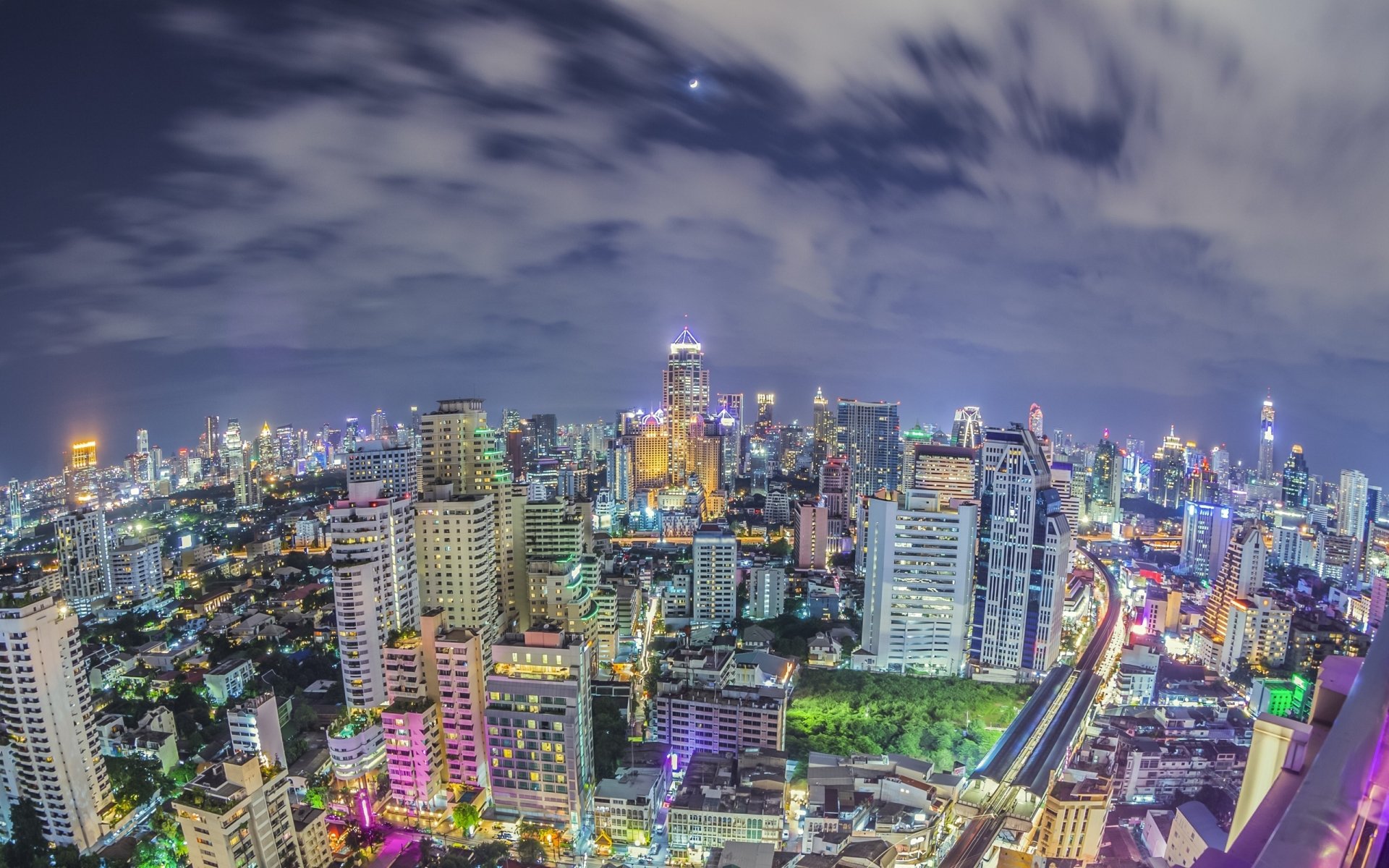 HD desktop wallpaper featuring a vibrant nighttime cityscape of Bangkok with illuminated skyscrapers and bustling streets under a cloudy sky.