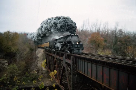 HD desktop wallpaper featuring a steam locomotive pulling a train on a bridge, with dense smoke billowing, set against a backdrop of autumn trees and cloudy sky.