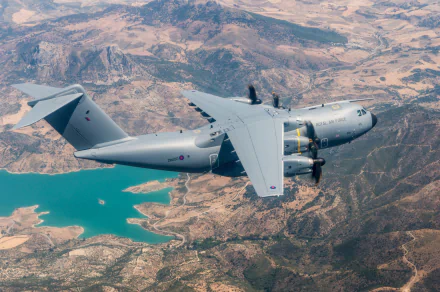 A military Airbus A400M transport aircraft flies above rugged terrain and a turquoise reservoir, captured in a high-definition desktop wallpaper.