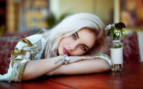 HD desktop wallpaper featuring a blonde woman model resting on a wooden table with a small flower vase, captured by Hakan Erenler.