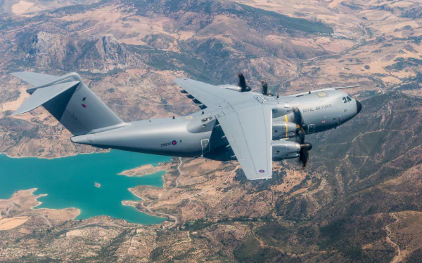 A military Airbus A400M transport aircraft flies above rugged terrain and a turquoise reservoir, captured in a high-definition desktop wallpaper.