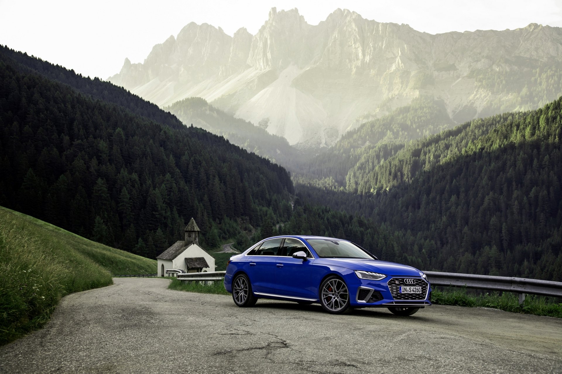 Blue Audi S4 compact car parked on a mountain road amid forested valleys and jagged peaks — 4K Ultra HD PC desktop wallpaper background.