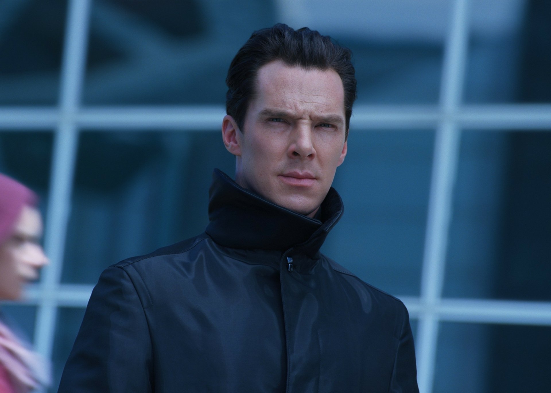 HD PC desktop wallpaper: stern man in dark coat gazes forward in a moody movie scene from Star Trek Into Darkness, blurred glass architecture forming the cool background.