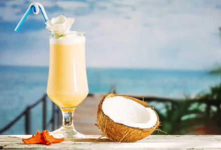 4K Ultra HD PC desktop wallpaper: tropical coconut drink/cocktail garnished with a flower, beside a halved coconut and starfish on a seaside table — food-themed beach background.