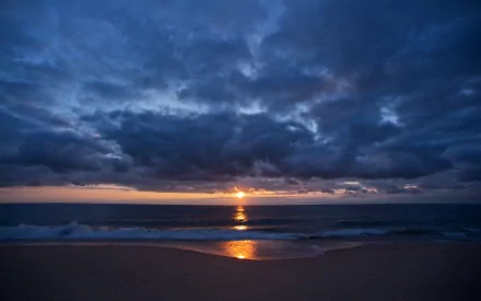 HD desktop wallpaper of a beach at sunrise with ocean waves, dramatic clouds, and natural colors reflecting on the water.