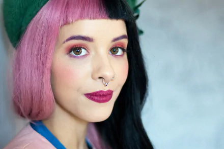 HD desktop wallpaper featuring American singer Melanie Martinez with distinctive half-pink, half-black hair, bold lipstick, and a septum piercing.