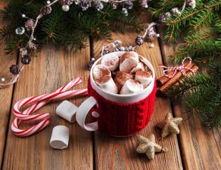 HD wallpaper featuring a festive cup of hot chocolate topped with marshmallows, cinnamon, and a candy cane, surrounded by Christmas decorations on a wooden table.