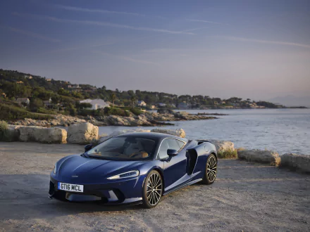 Blue McLaren GT supercar parked on a rocky seaside quay at sunset — sleek McLaren vehicle in high-detail 8K Ultra HD PC desktop wallpaper and background.