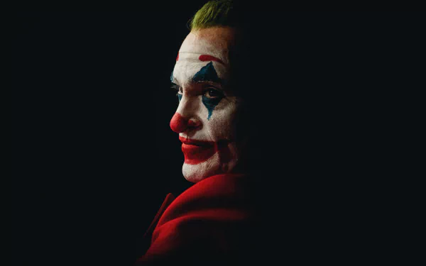 Moody close-up of the Joker from DC Comics in movie-style makeup and red suit, dramatic side lighting — 8K Ultra HD PC desktop wallpaper/background.