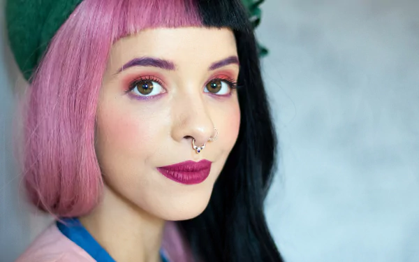 HD desktop wallpaper featuring American singer Melanie Martinez with distinctive half-pink, half-black hair, bold lipstick, and a septum piercing.