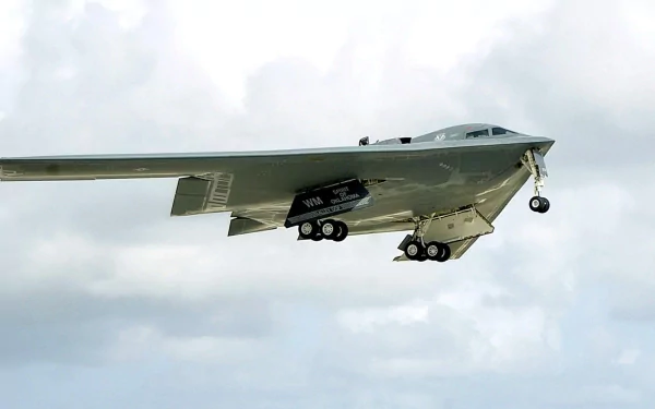 A Northrop Grumman B-2 Spirit stealth bomber in flight, showcasing its sleek design and advanced military technology against a cloudy sky. High-definition desktop wallpaper.