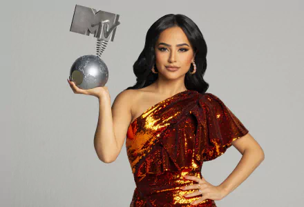 Becky G, American singer with black hair and brown eyes, wears sequin earrings and an orange sequin dress, holding an MTV award in this 4K Ultra HD desktop wallpaper.