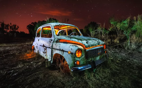 A rusted, wrecked Seat car sits abandoned in a dark, eerie field under a starry night sky, captured in stunning 4K Ultra HD resolution.