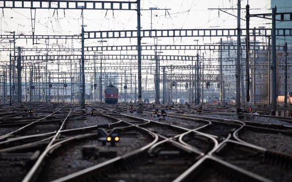 HD desktop wallpaper showing a complex network of railroad tracks and overhead wires in Zurich, Switzerland, with a train approaching in the distance.