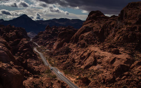 4K Ultra HD PC desktop wallpaper of a man-made paved road slicing through rust-red rocky desert toward distant mountains beneath brooding clouds.