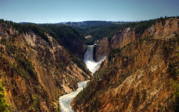 HD PC desktop wallpaper: Yellowstone Falls cascading through a steep canyon, river winding below amid rugged cliffs and forested rim — dramatic nature scene.
