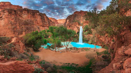 HD PC desktop wallpaper showcasing the vibrant turquoise waters and lush greenery of Havasupai Falls set against dramatic red canyon cliffs under a colorful sky.