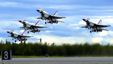 Four military jet fighters take off in a synchronized diamond formation during an air show, set against a backdrop of a clear blue sky. HD desktop wallpaper.