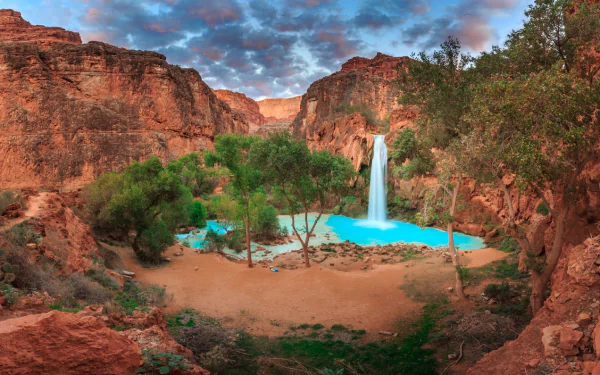 HD PC desktop wallpaper showcasing the vibrant turquoise waters and lush greenery of Havasupai Falls set against dramatic red canyon cliffs under a colorful sky.