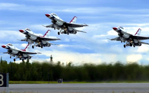 Four military jet fighters take off in a synchronized diamond formation during an air show, set against a backdrop of a clear blue sky. HD desktop wallpaper.