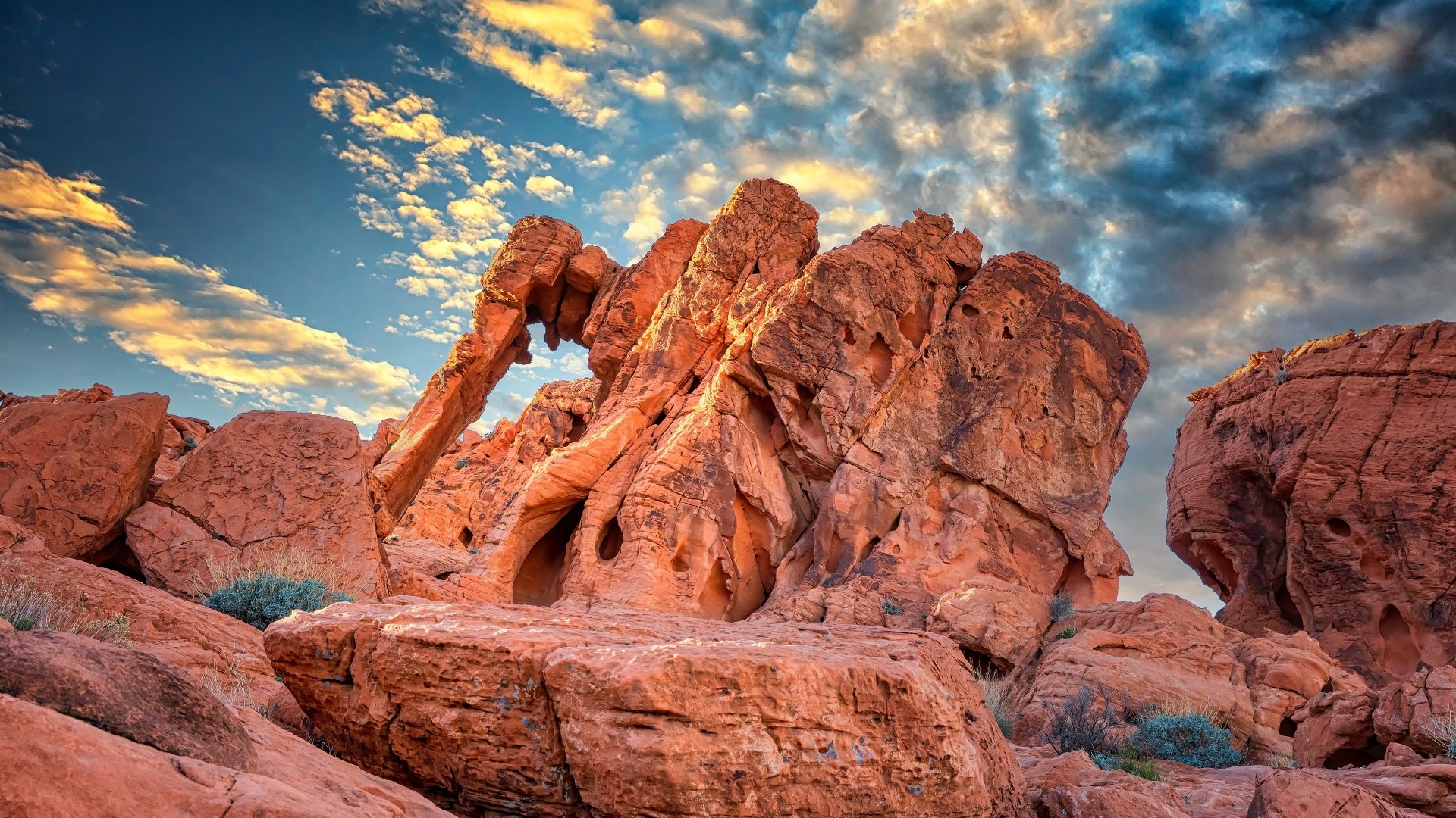 Nature rock arch in red sandstone — 4K Ultra HD PC desktop wallpaper background showing a rugged desert arch and boulders beneath a dramatic, cloud-filled sunset sky.