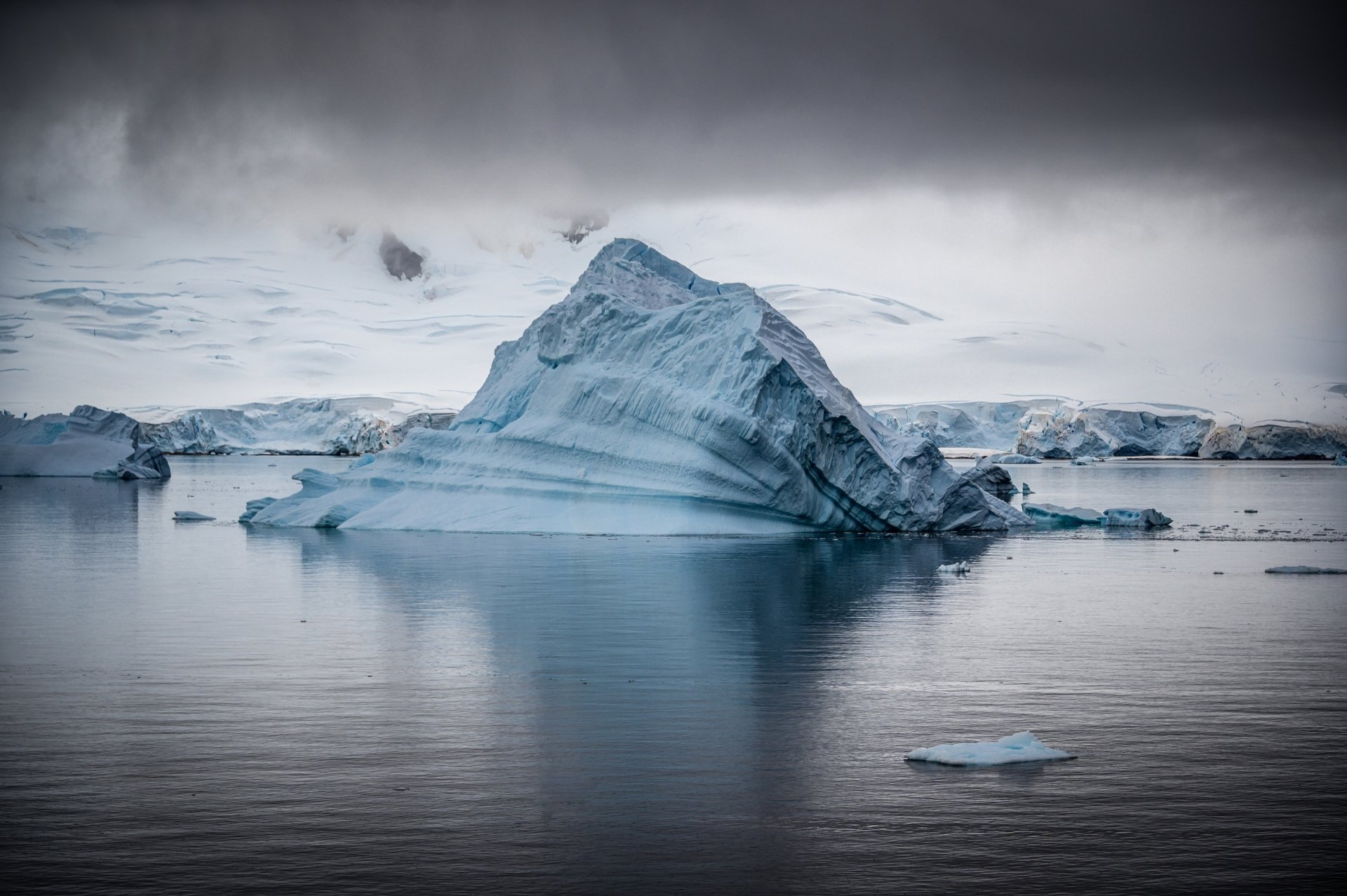 4K Ultra HD image of a large iceberg floating in the serene Antarctic sea, showcasing pristine nature and icy waters under a moody sky.