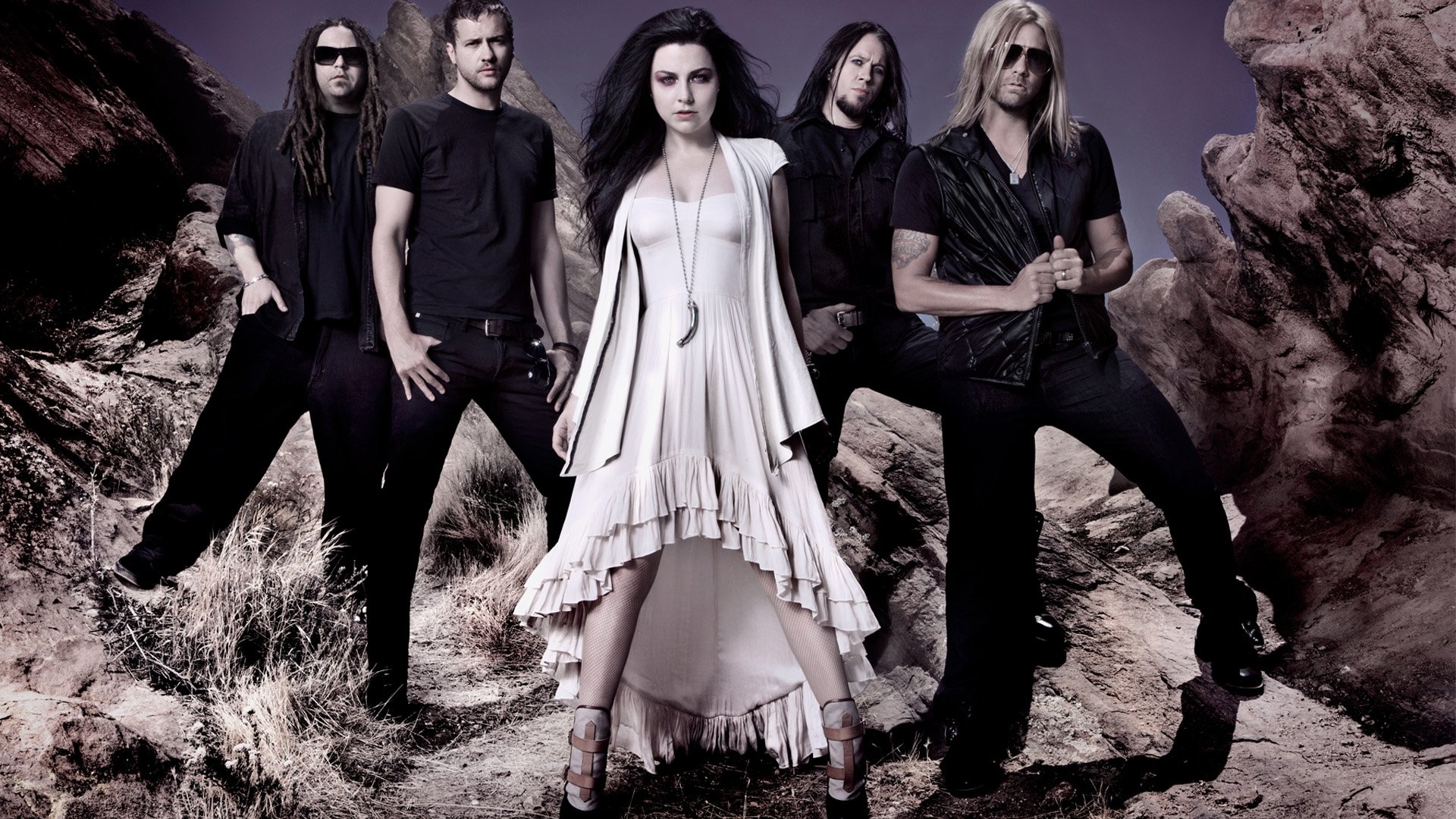 HD PC desktop wallpaper featuring the rock band Evanescence standing on rocky terrain with a moody, dark purple backdrop, emphasizing their music style.