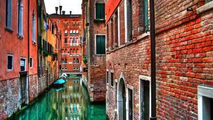 An HD desktop wallpaper featuring a picturesque canal in Venice, Italy, bordered by colorful, rustic buildings and boats on the emerald-green water.