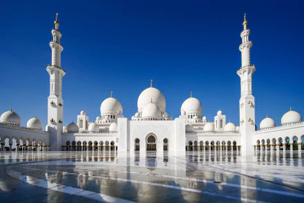Sheikh Zayed Grand Mosque in Abu Dhabi, United Arab Emirates, showcases stunning Islamic architecture with domes and minarets reflected on a glossy surface under a clear sky.