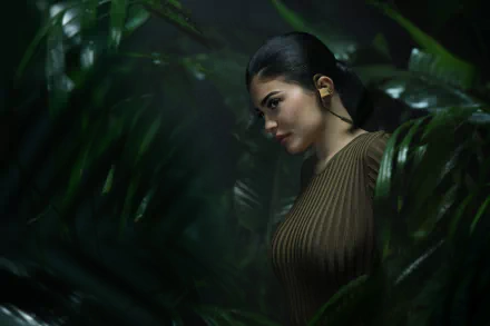 2K Quad HD desktop wallpaper: black‑haired female model in profile amid lush tropical foliage, sleek ponytail and ribbed top, moody cinematic lighting.