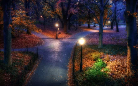 HD desktop wallpaper featuring a serene park with winding paths lit by vintage-style lampposts and surrounded by vibrant autumn foliage at dusk.