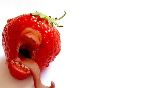 High-definition desktop wallpaper of a red strawberry with an unusual, open mouth and tongue detail, set against a white background.