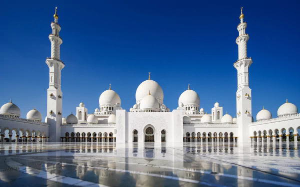 Sheikh Zayed Grand Mosque in Abu Dhabi, United Arab Emirates, showcases stunning Islamic architecture with domes and minarets reflected on a glossy surface under a clear sky.